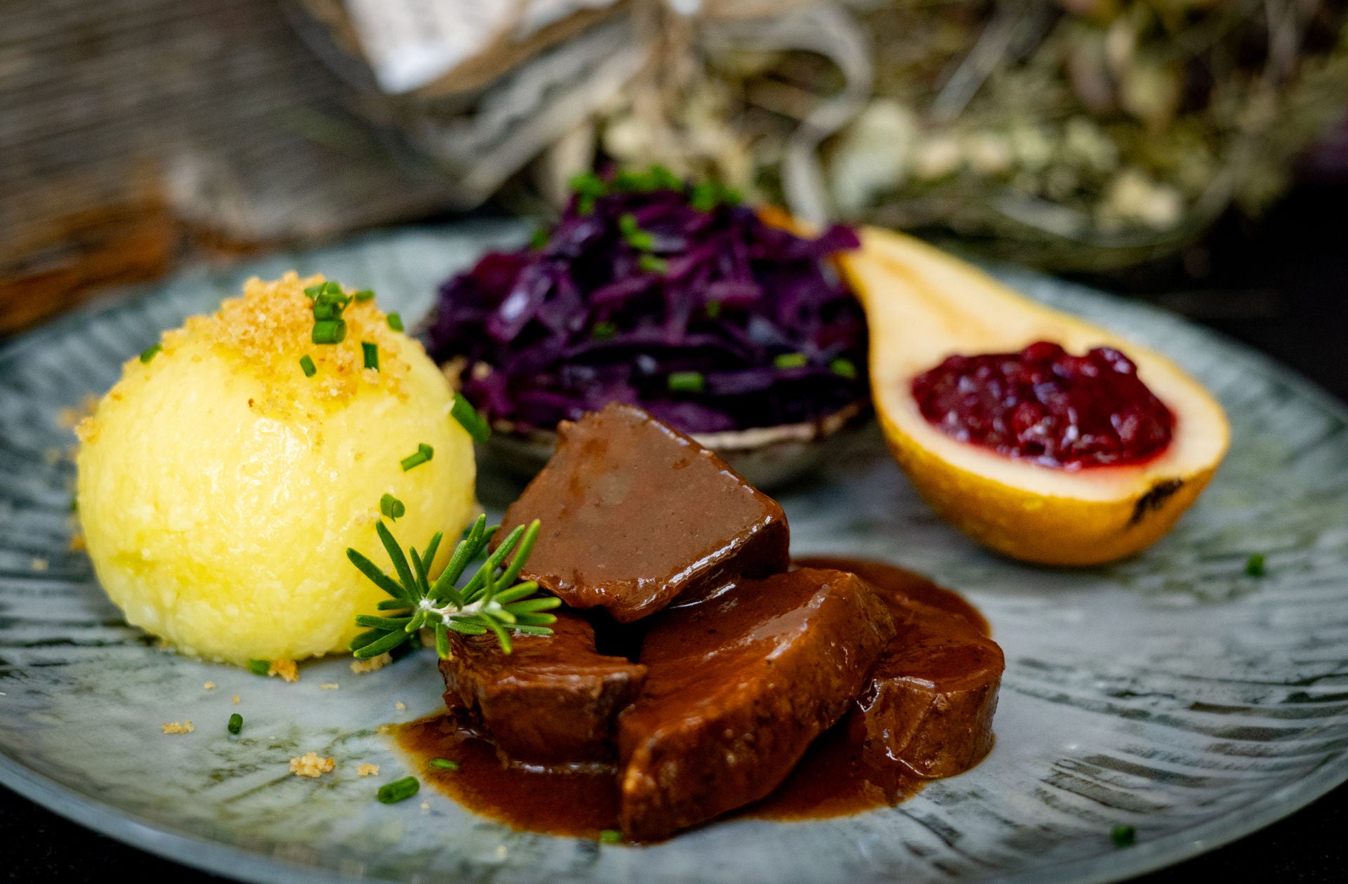 Rehbraten angerichtet auf einem Teller mit Rotkraut, Knödel, Birne und Preiselbeermarmelade