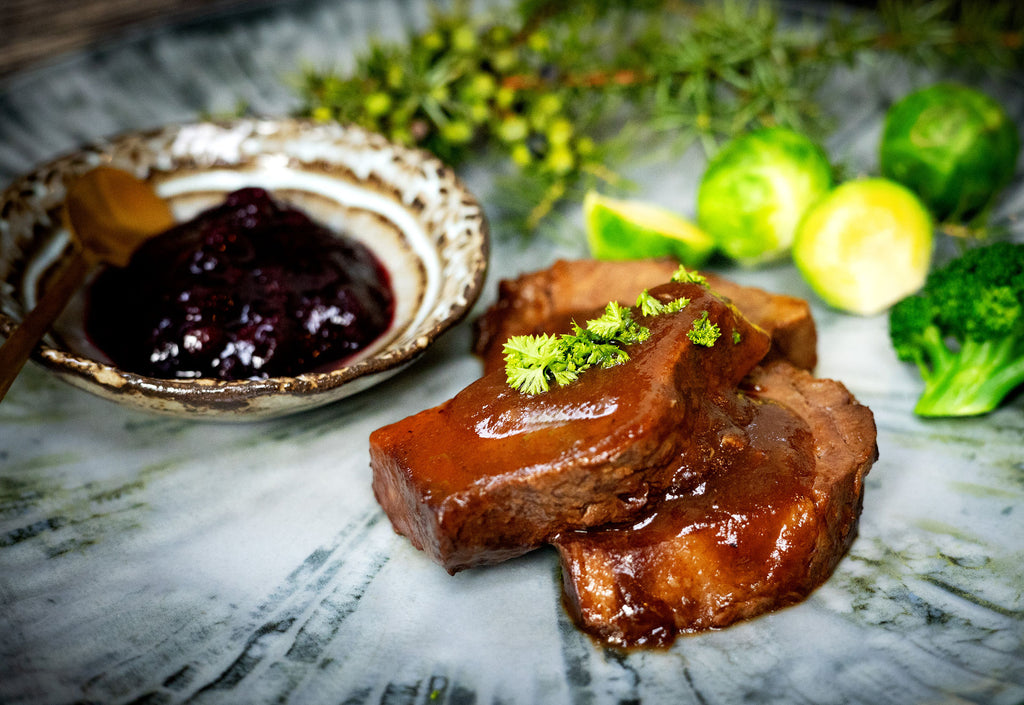 Hirschbraten angerichtet auf einem Teller mit Rosenkohl, Brokkoli und Preiselbeermarmelade