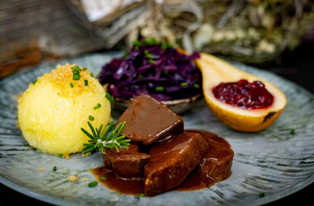 Rehbraten angerichtet auf einem Teller mit Rotkraut, Knödel, Birne und Preiselbeermarmelade