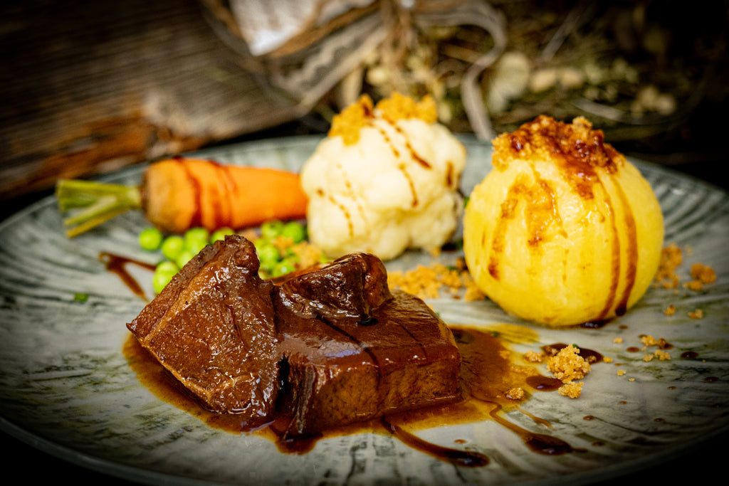 Sauerbraten auf dem Teller angerichtet mit einem Knödel, Blumenkohl, Möhre und Erbsen